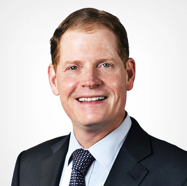Professional headshot of a smiling man in a suit and tie against a plain white background.