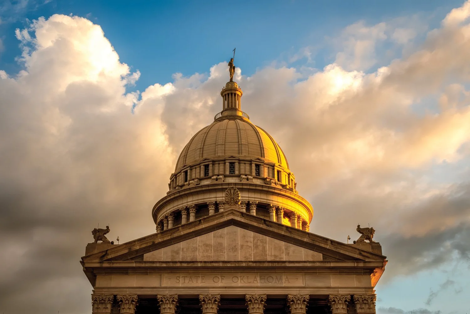 Golden-domed capitol building with statues on the roof and cloudy sky in background, Oklahoma State Capitol.