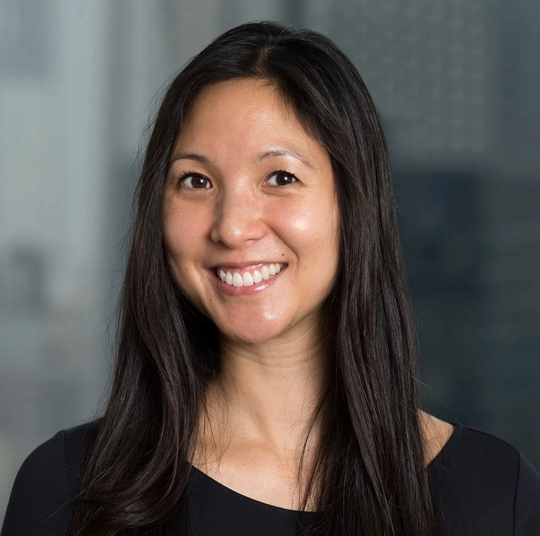 A woman with long dark hair smiling in an indoor setting with a blurred background.