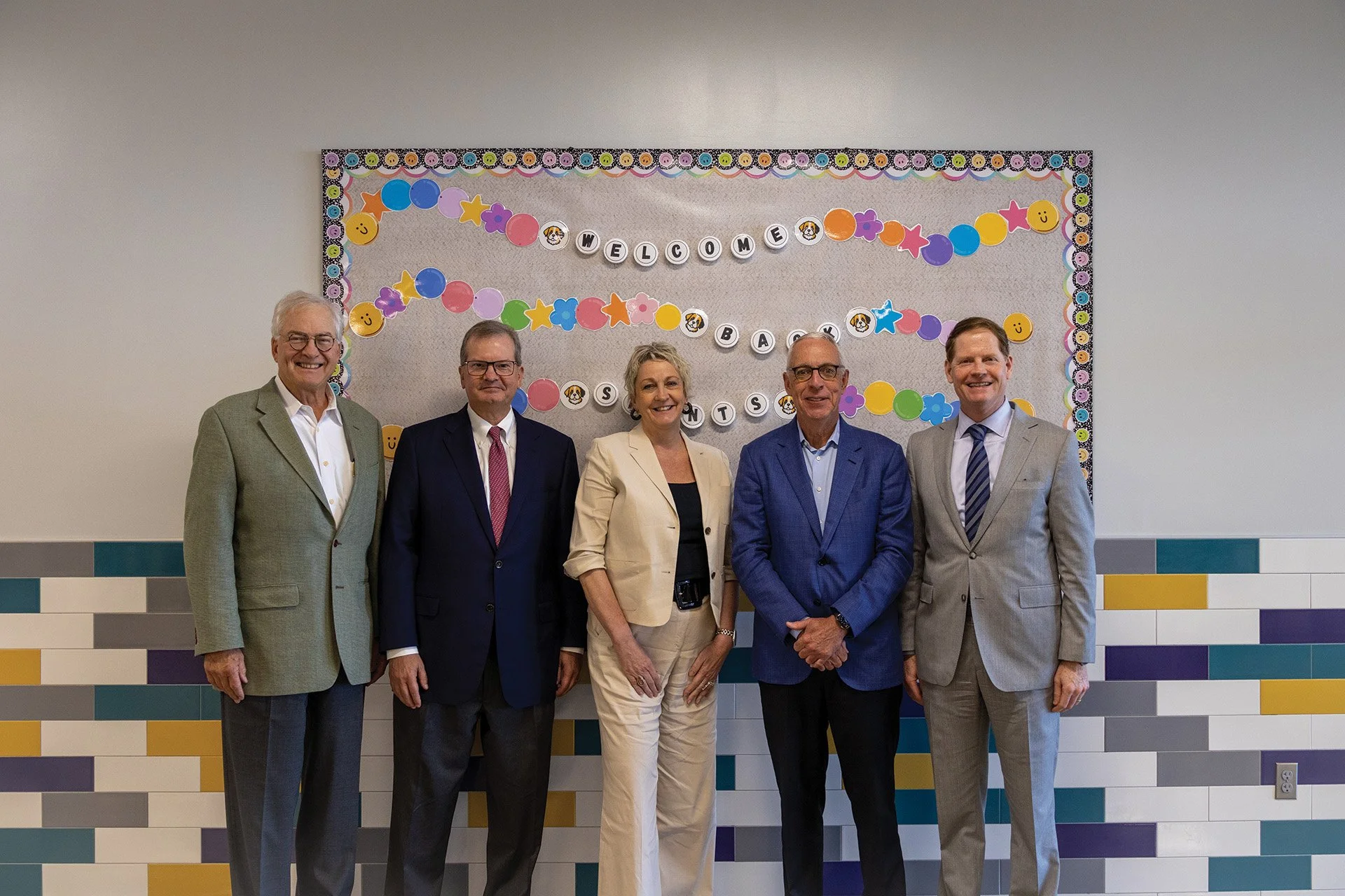 Group of five professionally dressed adults standing in front of a colorful 