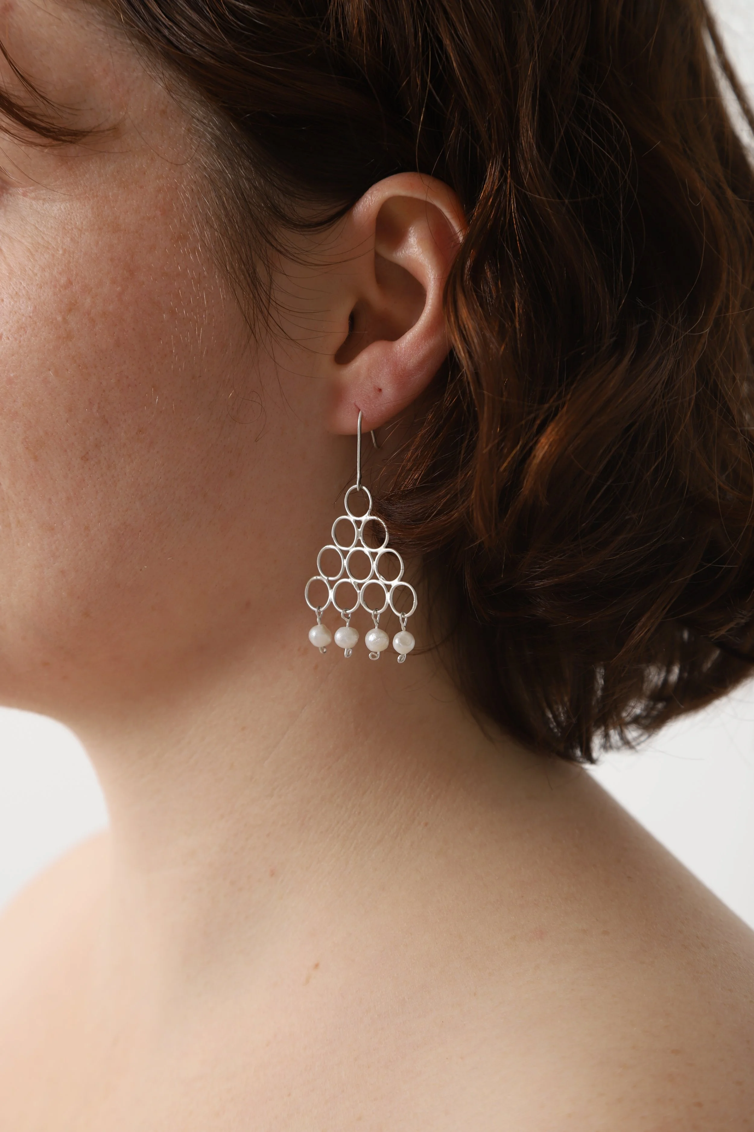 Aretes plateados con diseño de círculos y perlas blancas colgando.