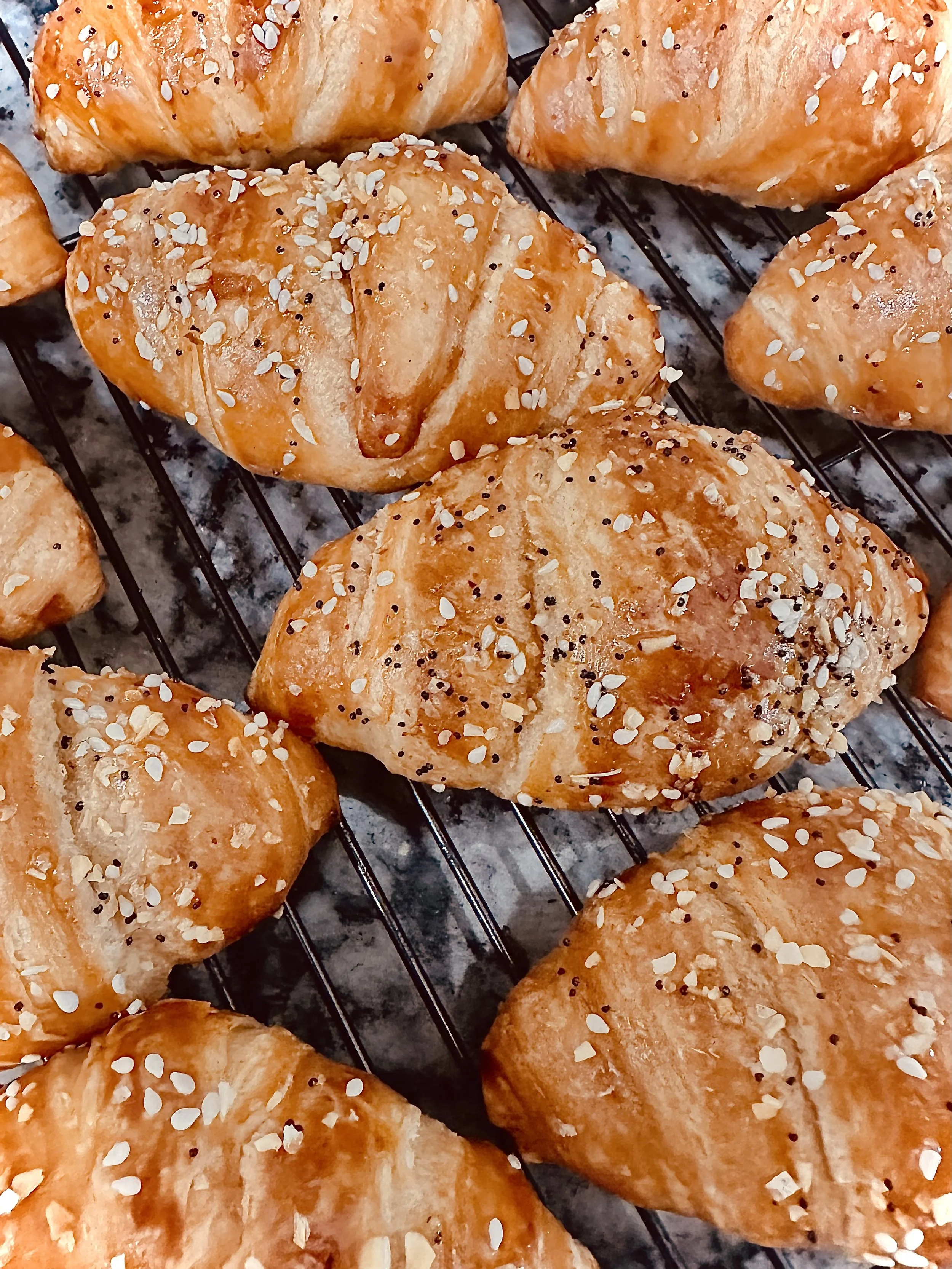 Freshly baked croissants topped with sugar and seeds cooling on a wire rack.