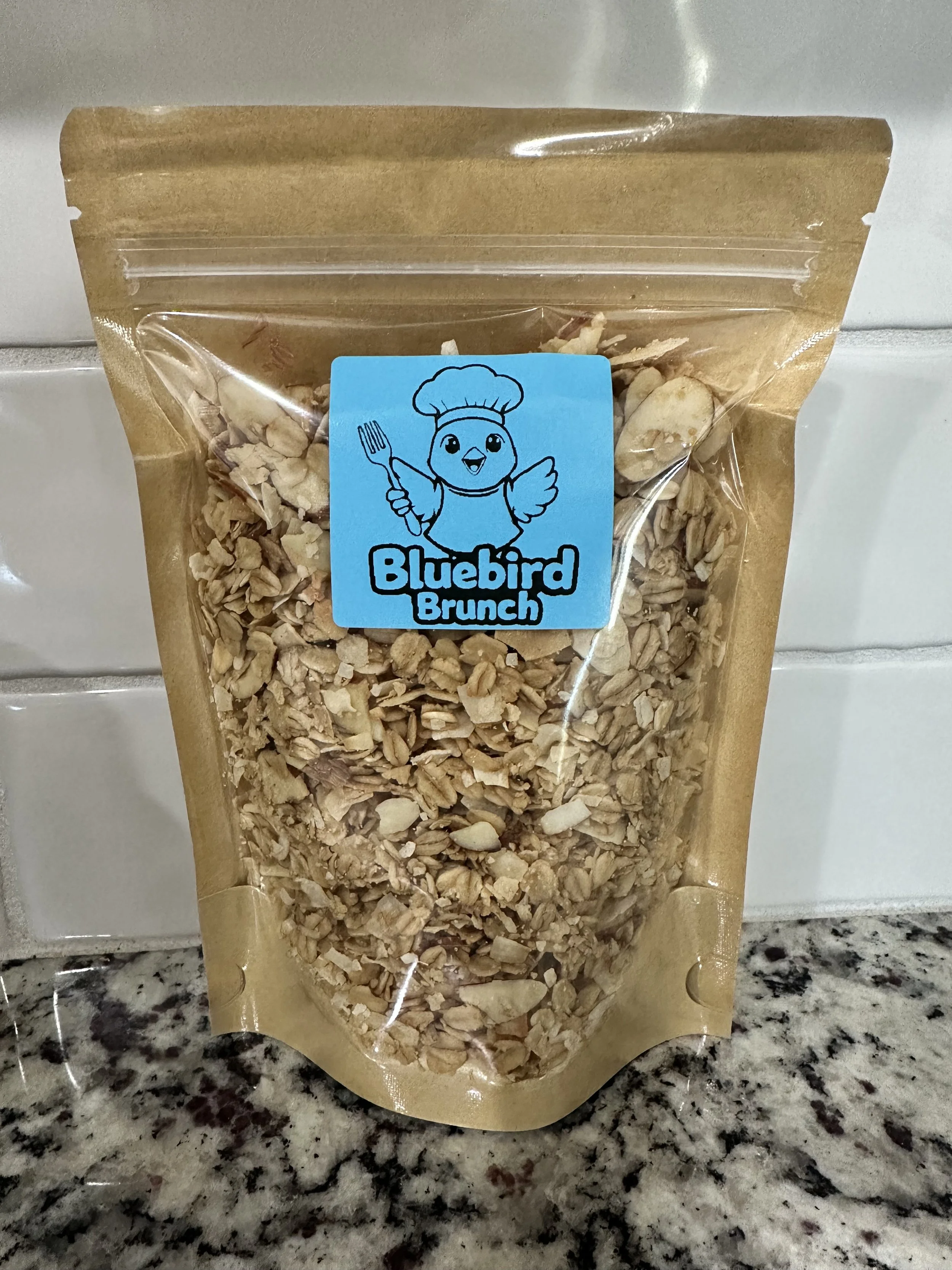 A brown resealable bag of granola with a blue label featuring a cartoon bird wearing a chef's hat, holding a fork, and the text 'Bluebird Brunch'.
