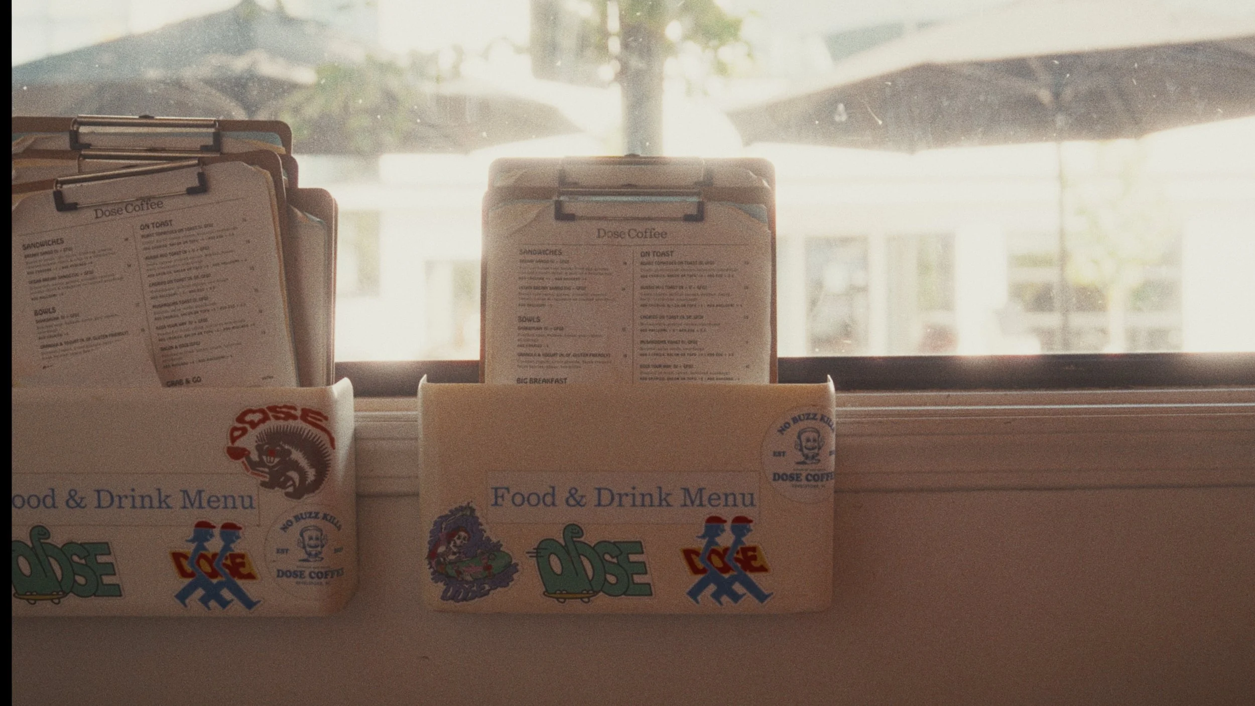 Two paper food and drink menus placed on a window sill with a street scene background.