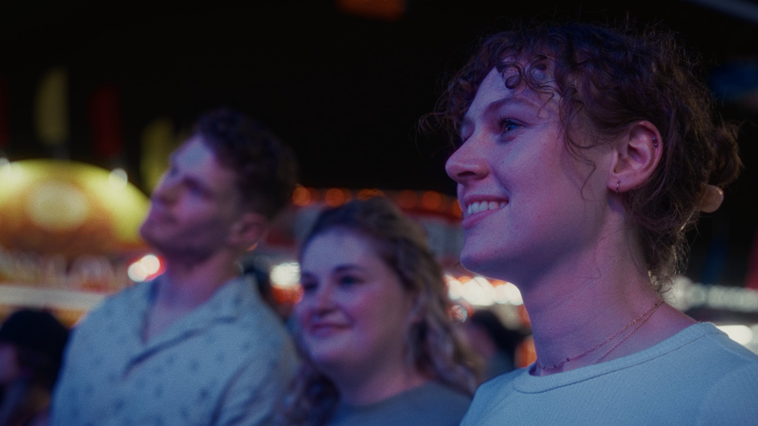 A group of people at a nighttime amusement park or carnival, smiling and enjoying the scene.