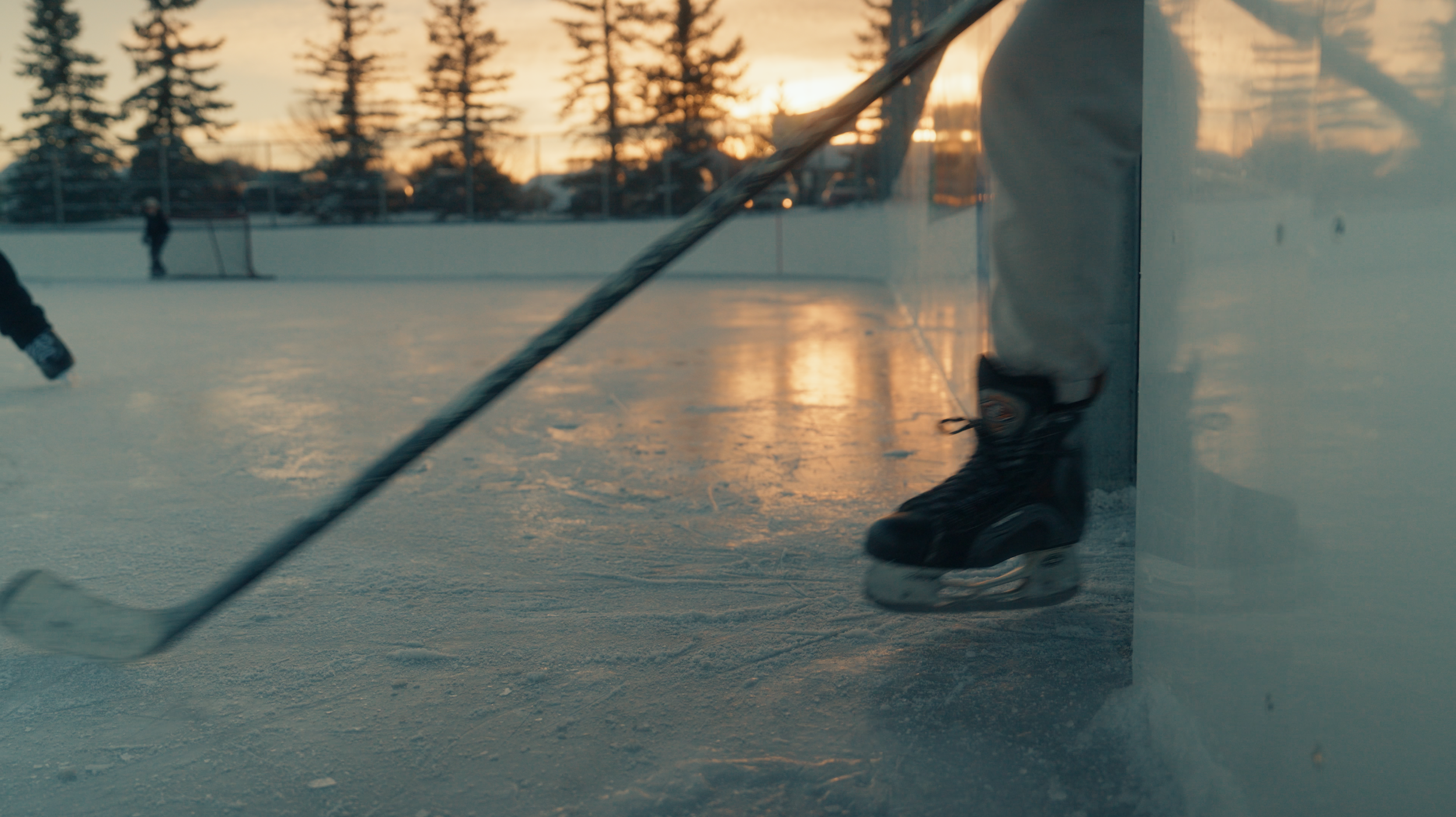 Close-up of an ice hockey player’s skates on the ice near the goal post during sunset at an outdoor ice rink.