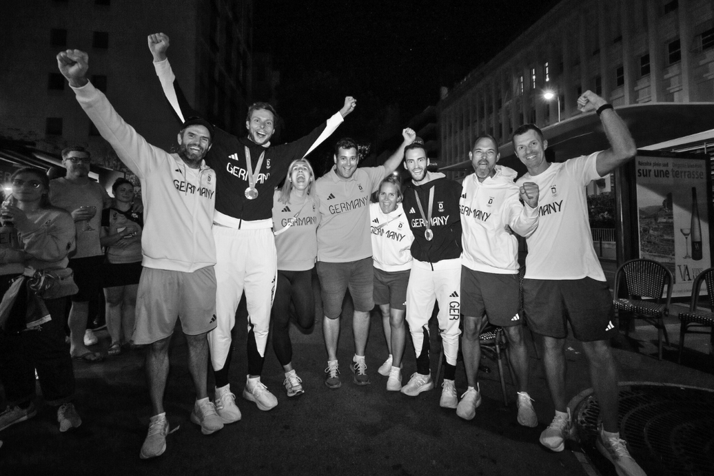 Deutsche Athleten jubeln mit erhobenen Armen auf der Straße, Sie tragen Medaillen und Sportbekleidung mit Deutschland-Logo, nachts.
