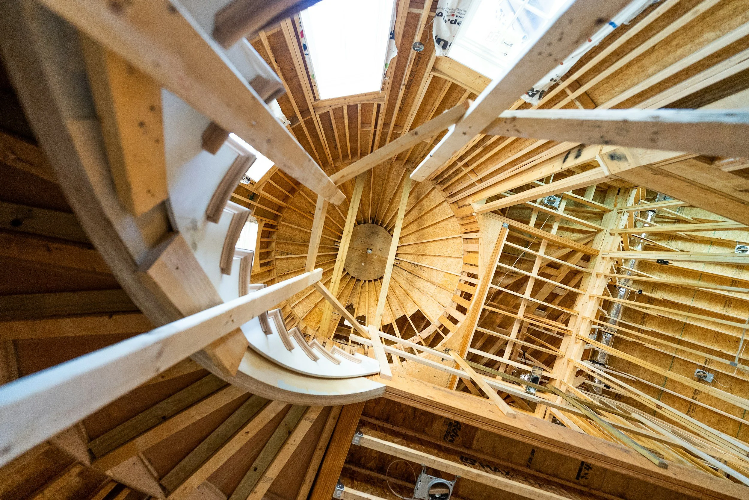 View looking down a circular wooden staircase under construction, showing wooden beams and framing.