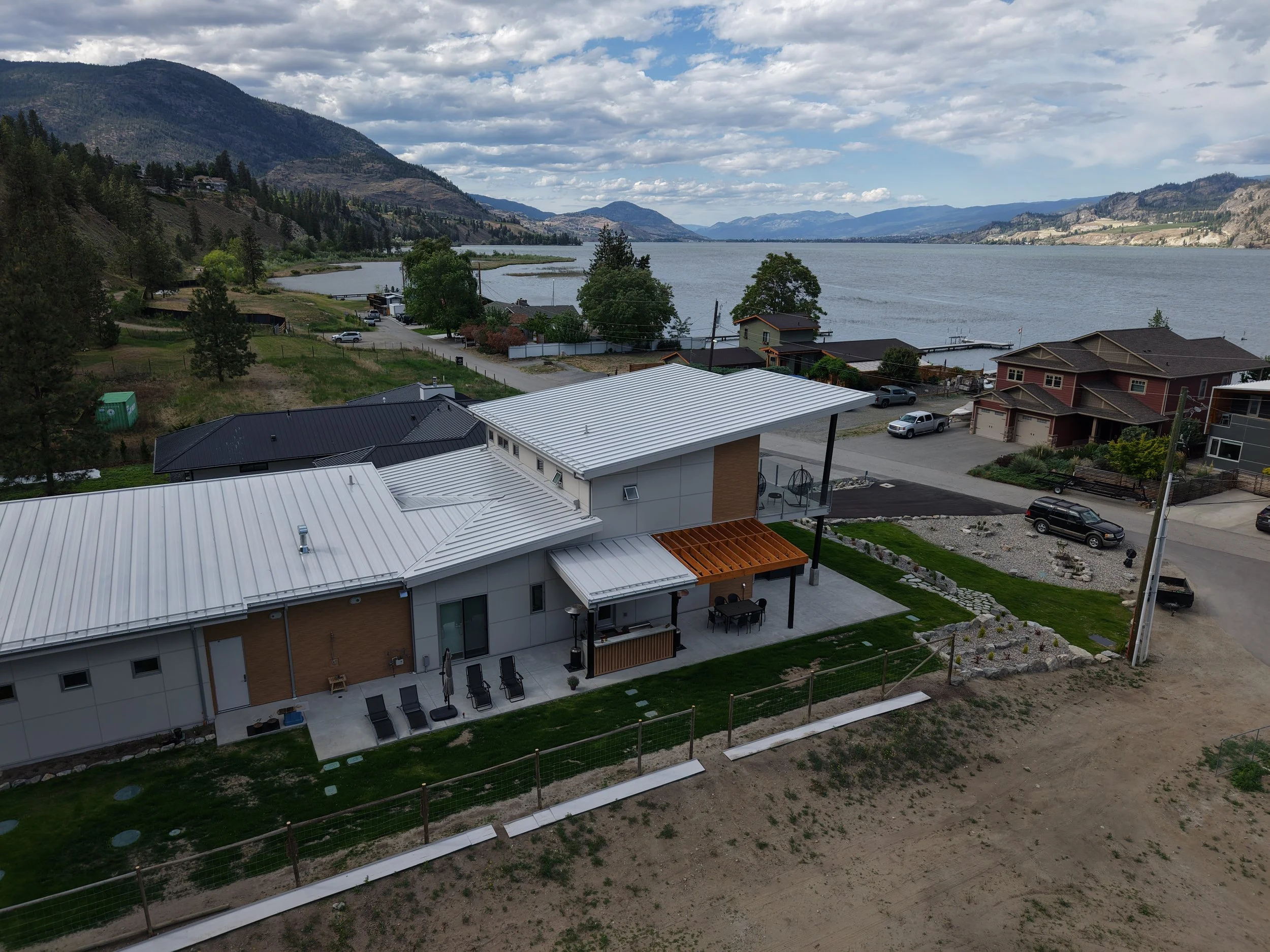 A lakeside residential area with houses, a large body of water, mountains in the background, and partly cloudy skies.