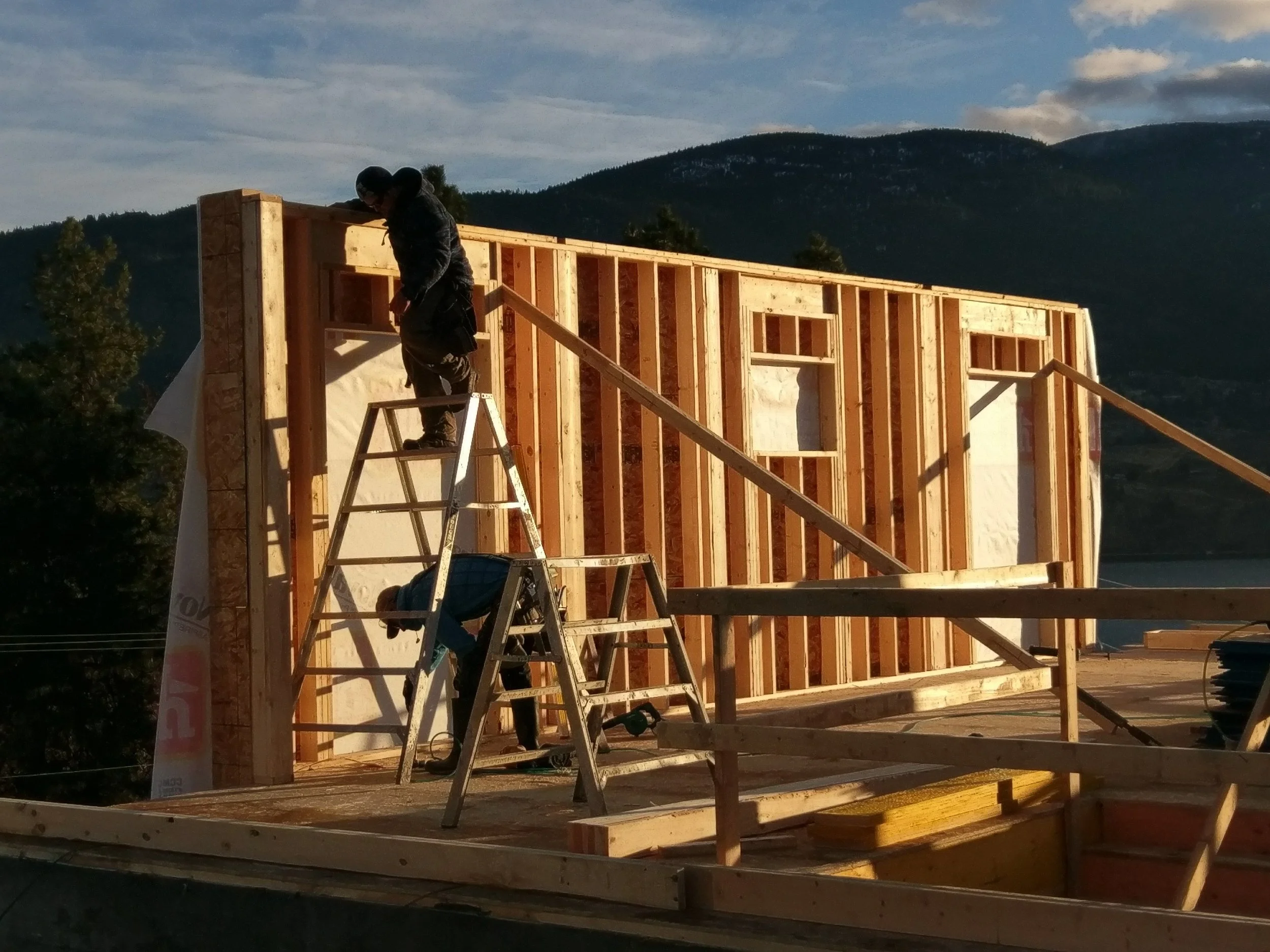 Construction workers building a wooden house frame outdoors with mountains in the background.