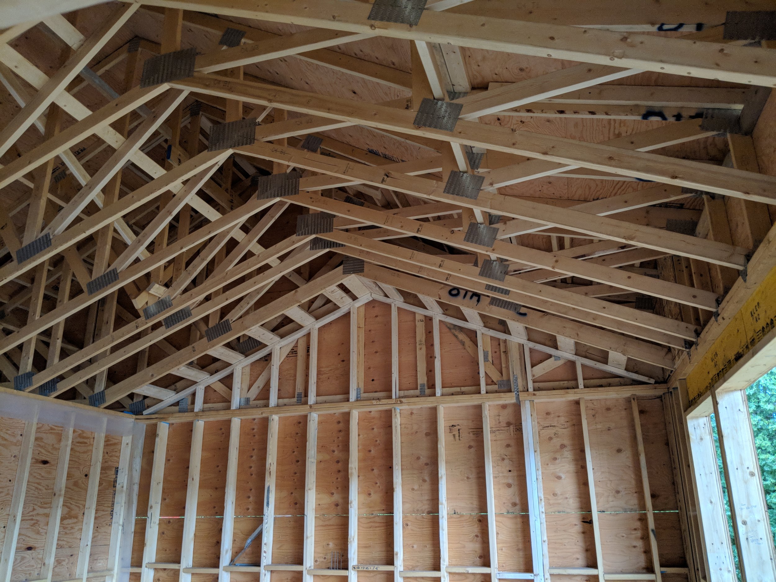 Interior view of a building under construction with wooden framing, exposed beams, and plywood wall sheathing.