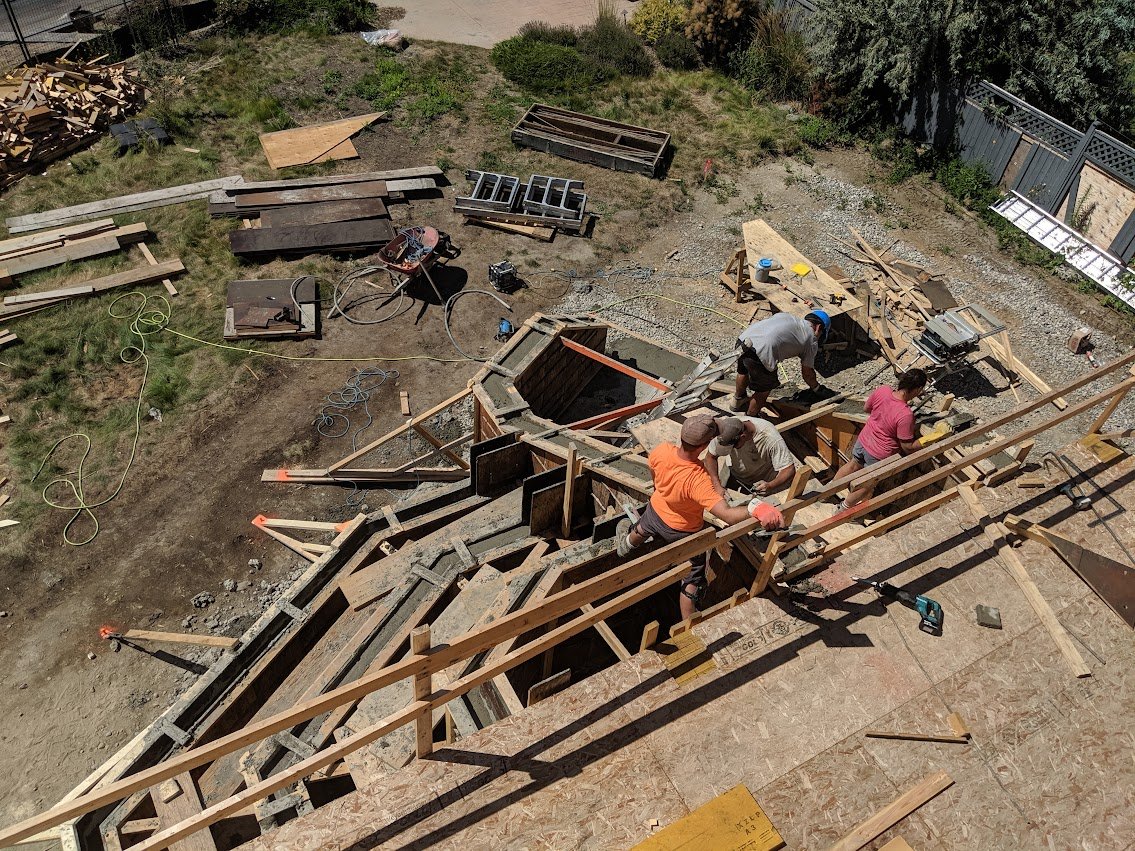 Construction site with workers building a wooden staircase or deck, surrounded by construction materials and tools.