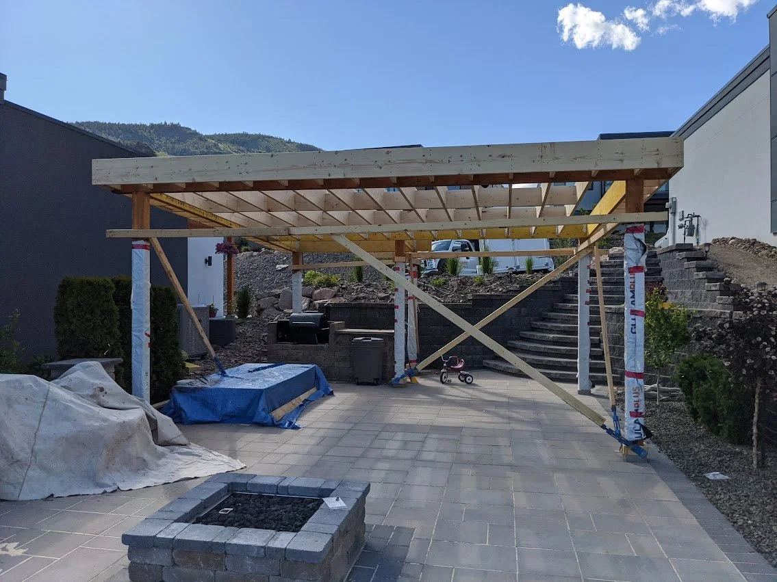 Construction of a wooden pergola over a paved patio area at a residential backyard.