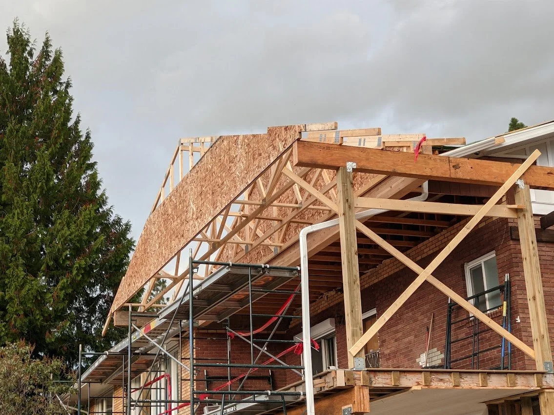 Building under construction with wooden framework and brick exterior, scaffolding and scaffolding supports in place.