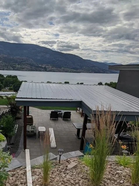 Outdoor patio with seating, overlooking a body of water and mountains under a cloudy sky.