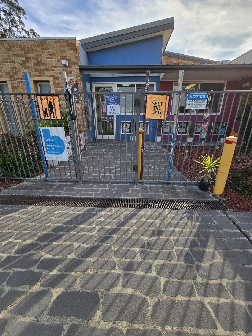 A gated entrance to a child care or learning center with signs that say "SHUT THE GATE" and 