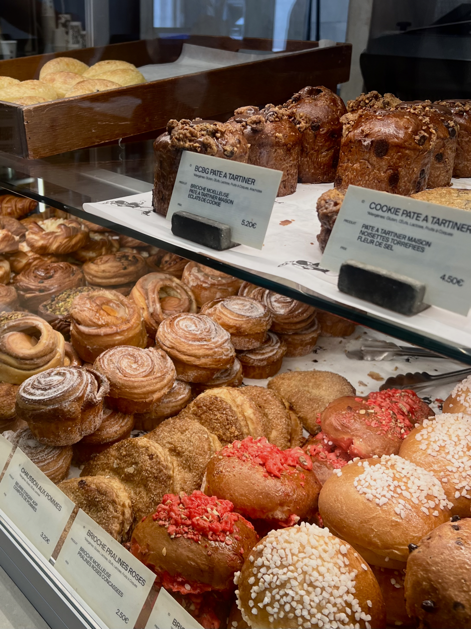 Display case of assorted baked goods including croissants, cinnamon rolls, and decorated sweet buns at a bakery.