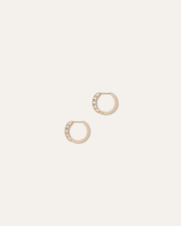 A pair of gold hoop earrings with small decorative stones on a light beige background.