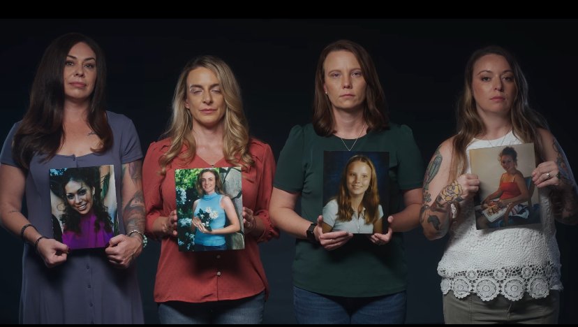 Four women stand against a dark background, each holding a photograph of a young girl.