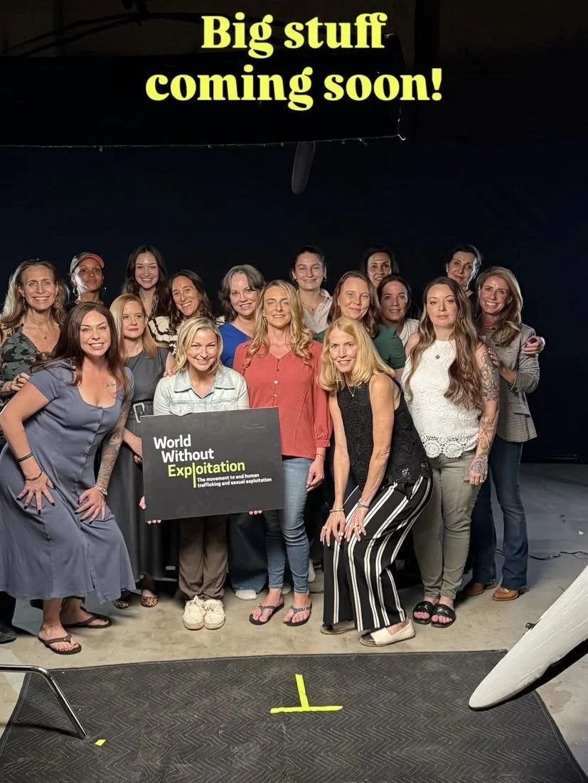 Group of women holding a sign that reads 'World Without Exploitation' at an event against human trafficking and sexual exploitation, with a banner above that says 'Big stuff coming soon!'