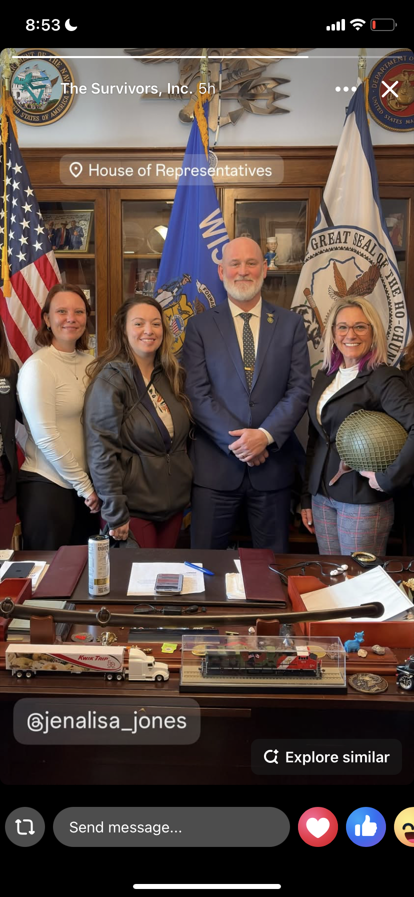 Four people standing in front of flags and emblems at the House of Representatives, with a large wooden desk in the foreground.