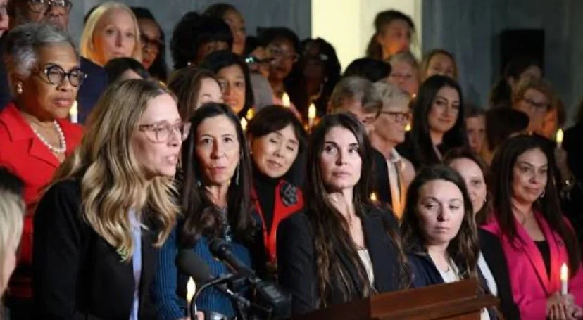 A diverse group of women attending a formal event, some speaking into microphones, others listening, with candles in the background.