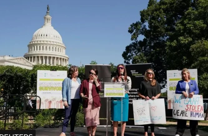 Group of women speaking at a protest in front of the U.S. Capitol building, holding signs about climate change, human rights, and social issues.