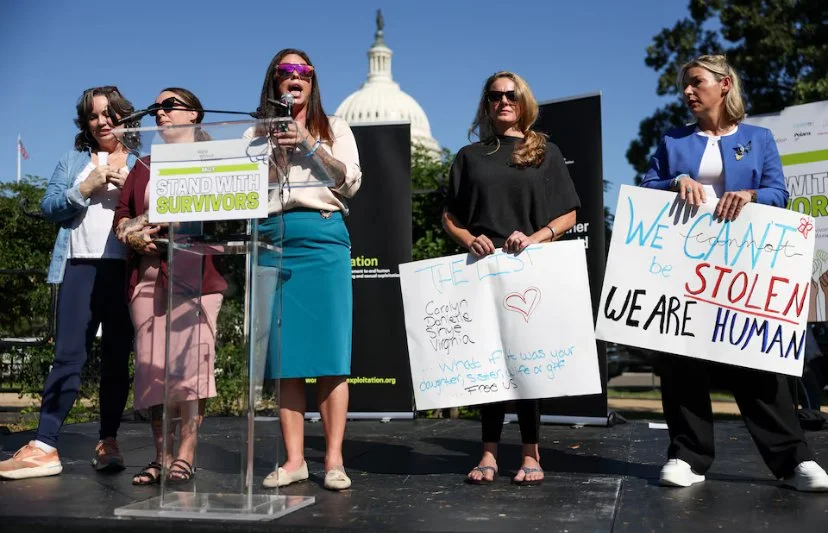 Group of women protesting at a rally, holding signs with messages about survivors and human rights, with the Capitol building in the background.