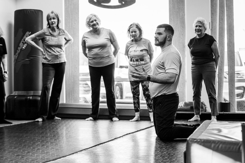 Bryan DePhillip kneeling on the mat while explaining a protective movement to a group of older adults
