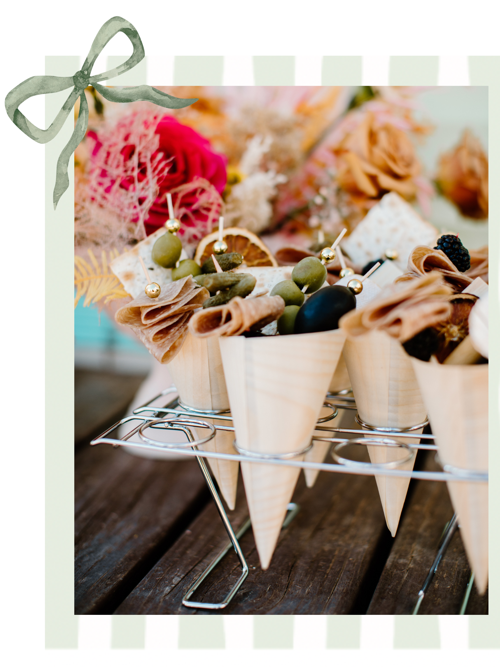 Appetizer cones with assorted cured meats, olives, and garnishes on a wooden table, with a decorative ribbon in the corner.