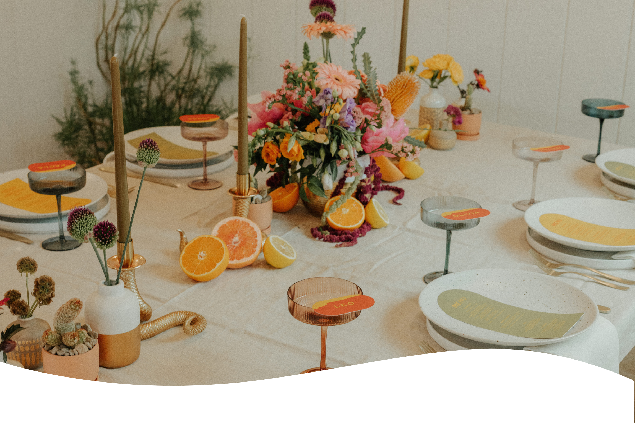 A table decorated with a floral centerpiece, sliced citrus fruits, candles, and name cards for a meal setting.