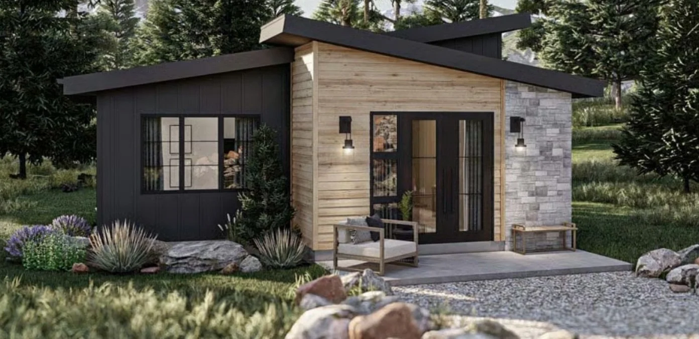 A modern small house with a mix of black, wood, and stone exterior, surrounded by greenery and rocks, featuring a front porch with a bench and outdoor lighting.
