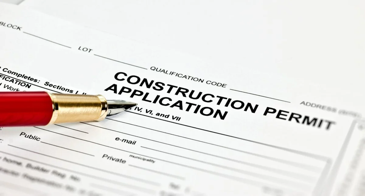 Close-up of a construction permit application form with a red and gold pen resting on it.