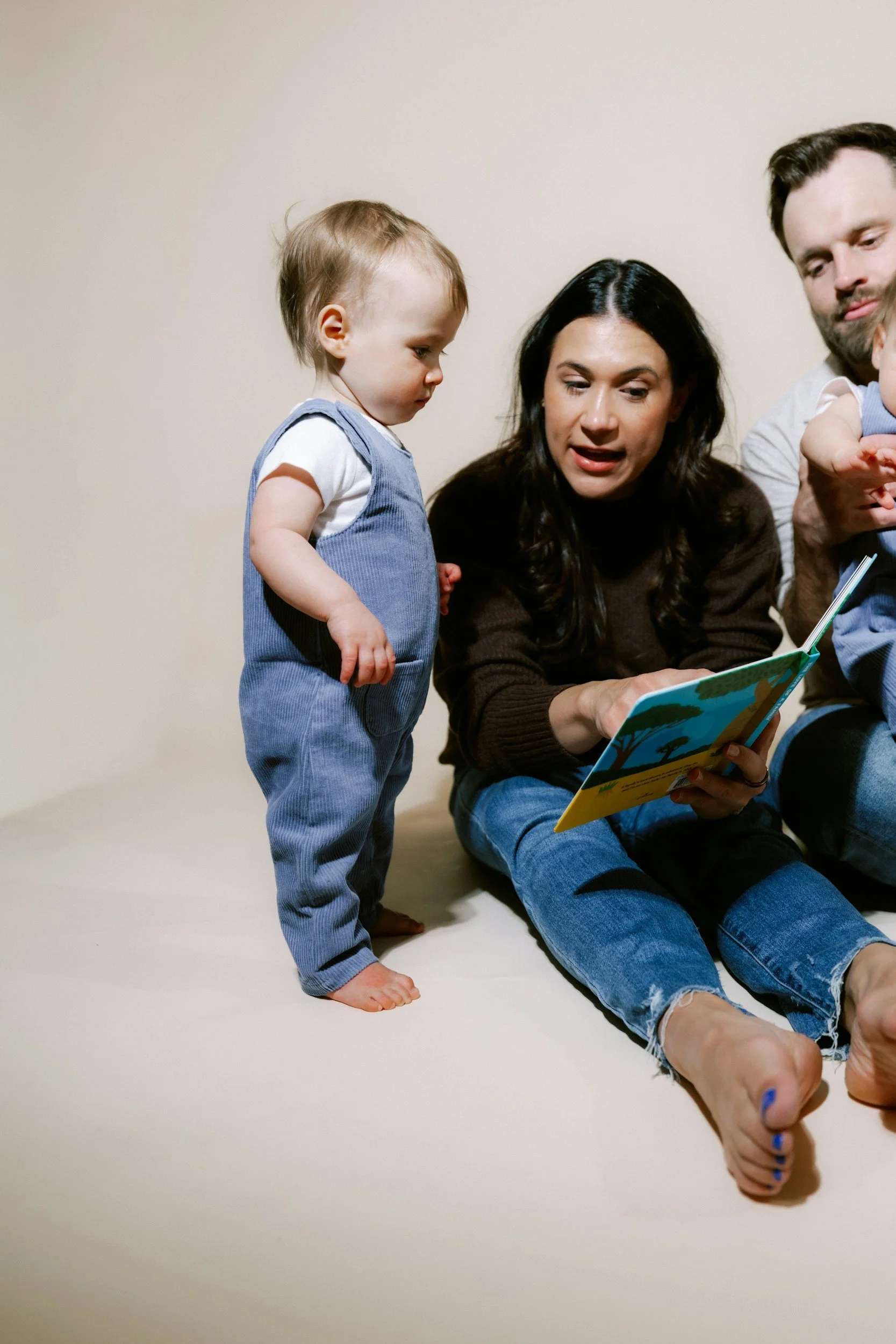 A woman and two small children sitting on the floor, looking at a colorful picture book.