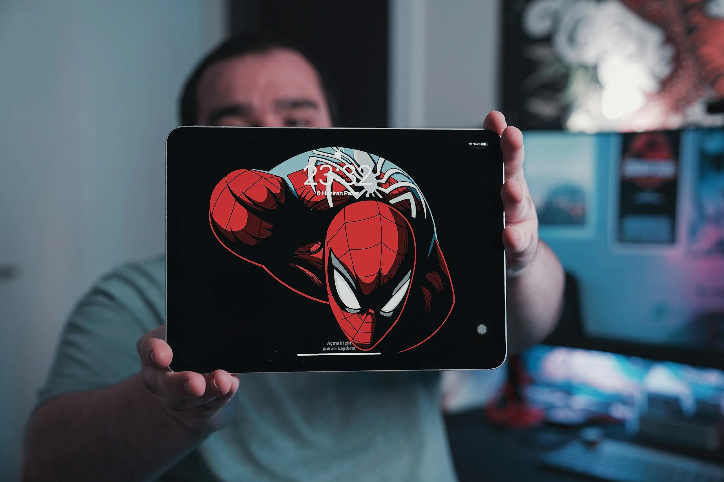 Person holding a tablet displaying a Spider-Man wallpaper with a cartoon illustration of Spider-Man's face in front of a blurred background.
