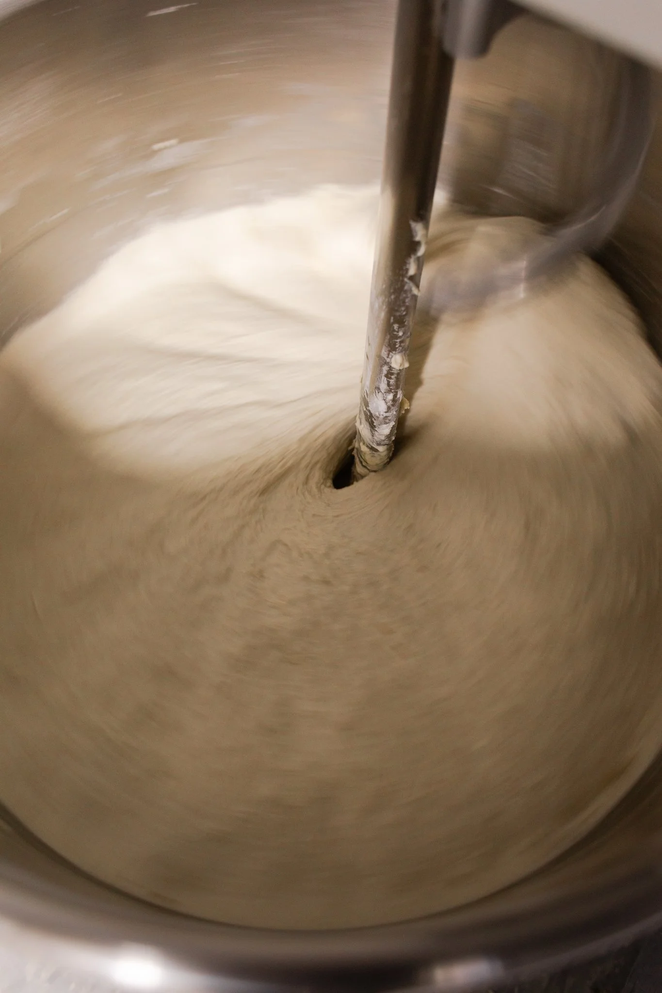 A mixer blending dough in a metal mixing bowl.