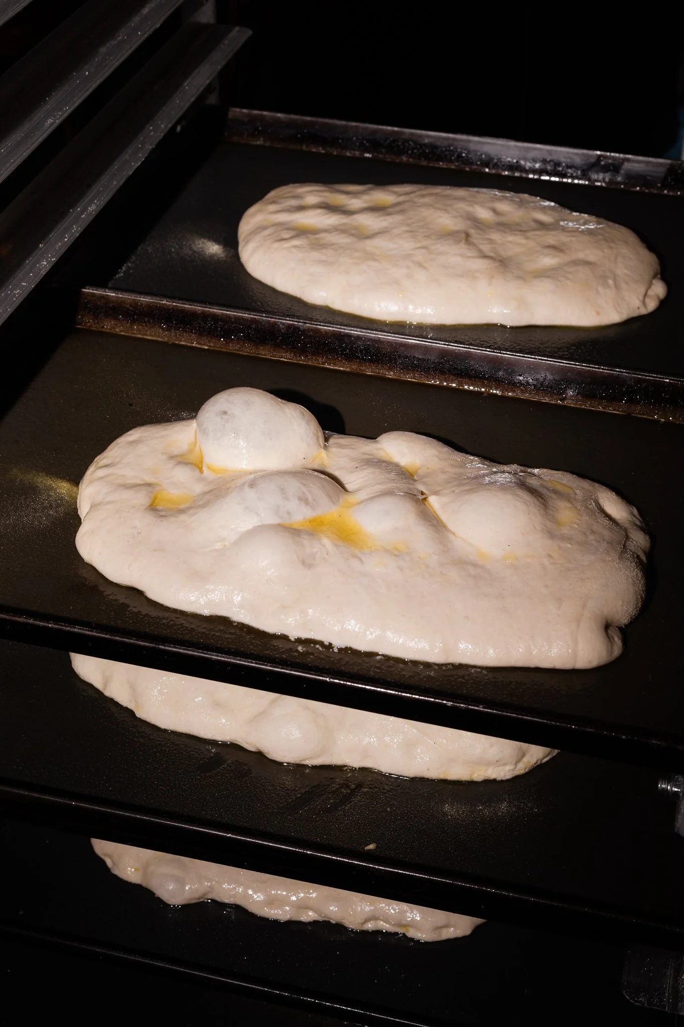 Pizzas baking inside an oven on baking sheets, with crust rising.
