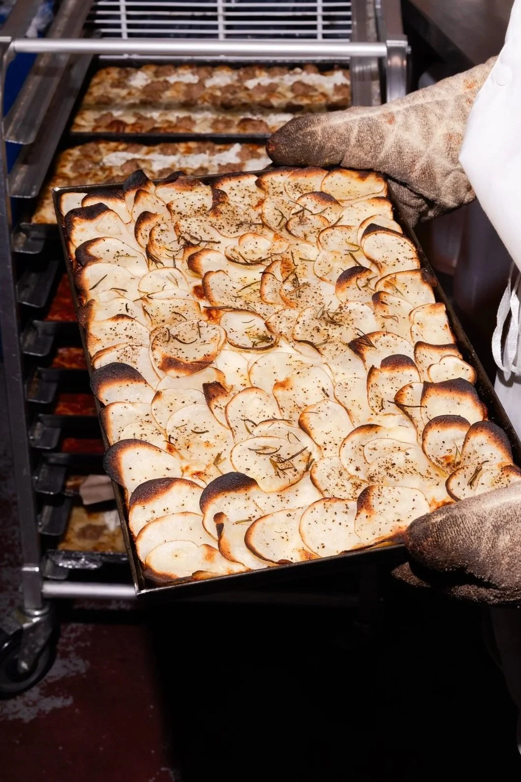 Pizza tray of freshly roasted potato slices garnished with herbs, straight out of the oven.