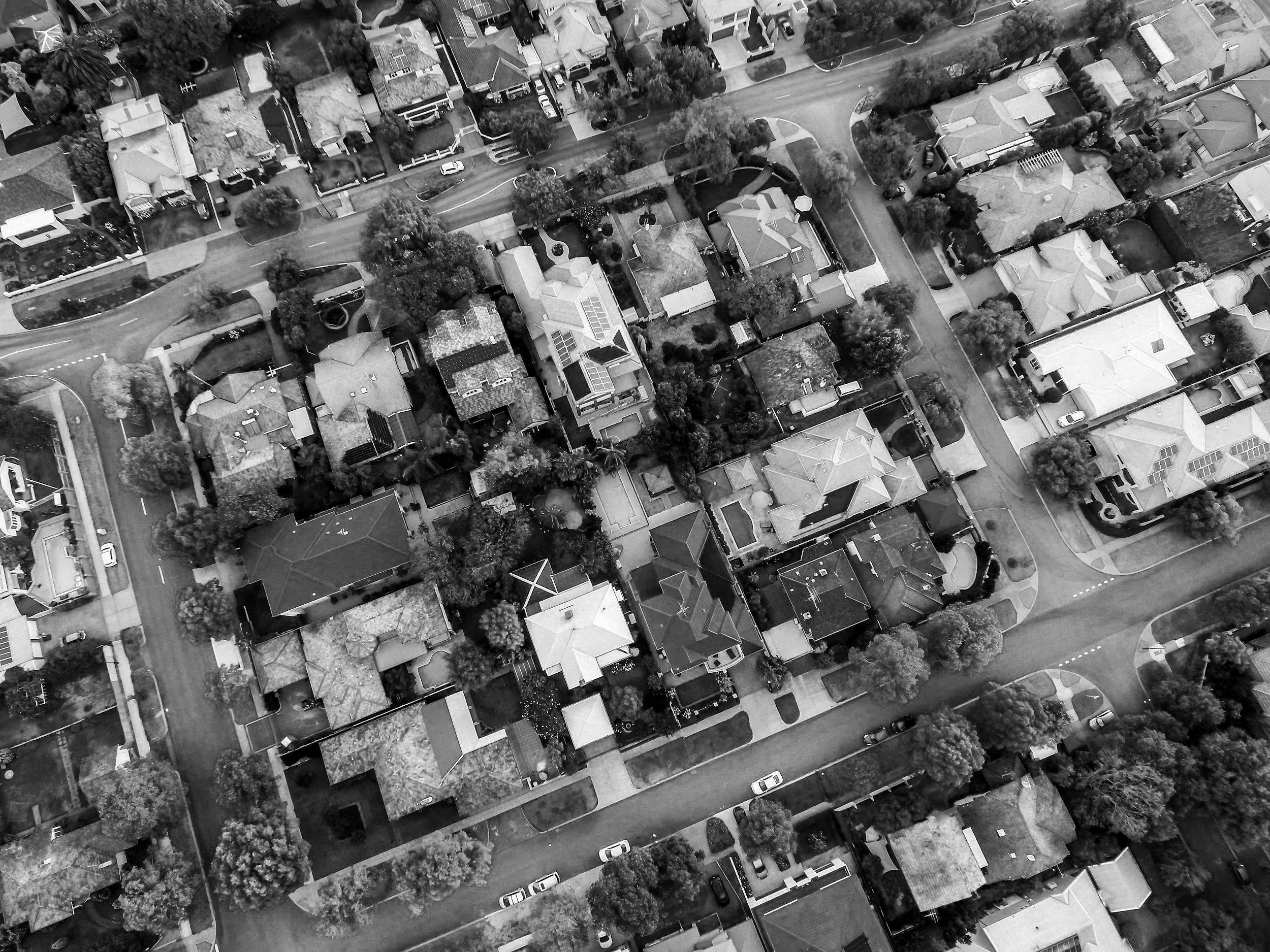 An aerial view of a residential neighbourhood with houses, streets, trees, and parked cars.
