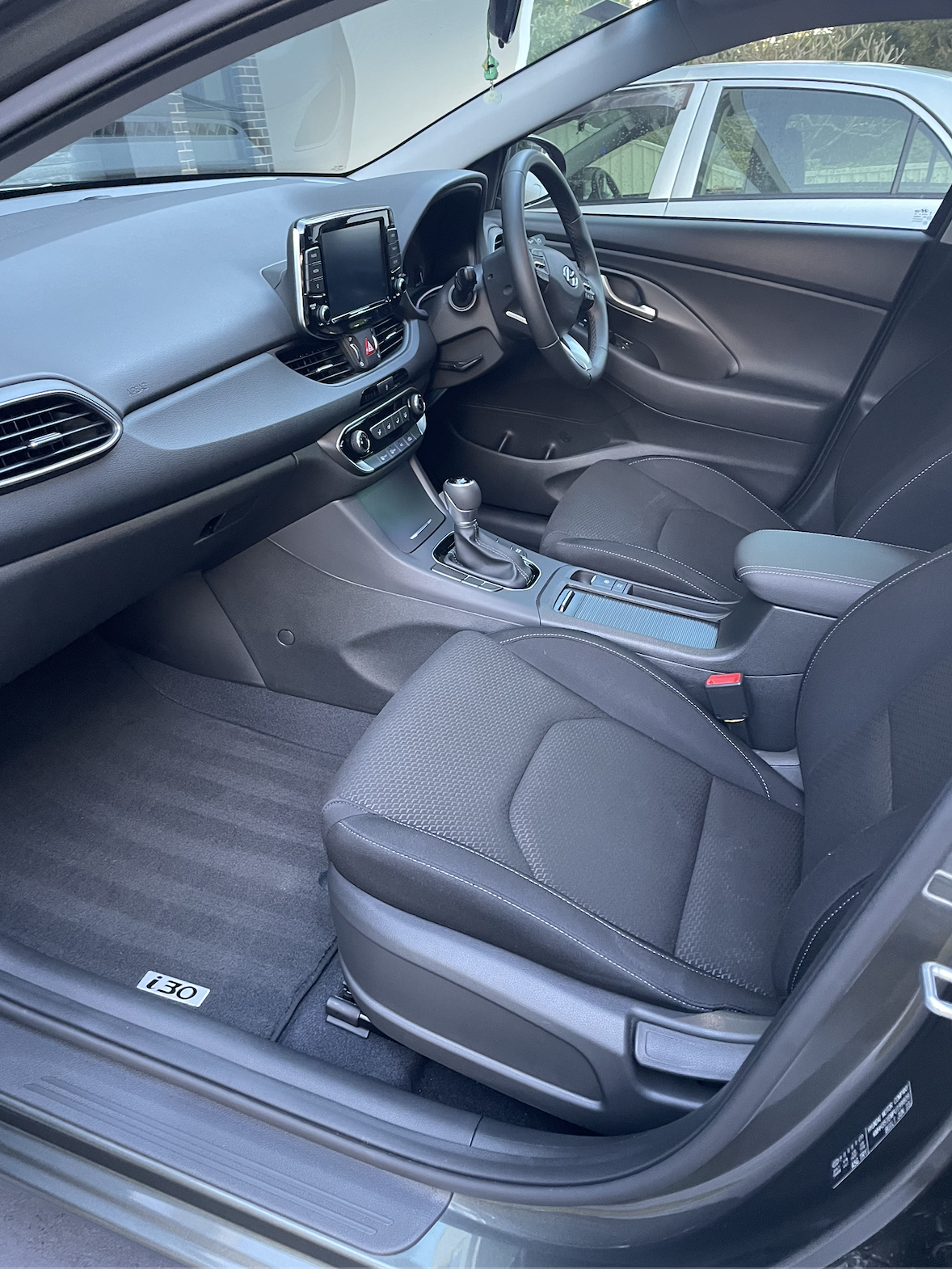 Interior of a modern car showing the driver's seat, steering wheel, dashboard, center console with gear shift, and front passenger seat.