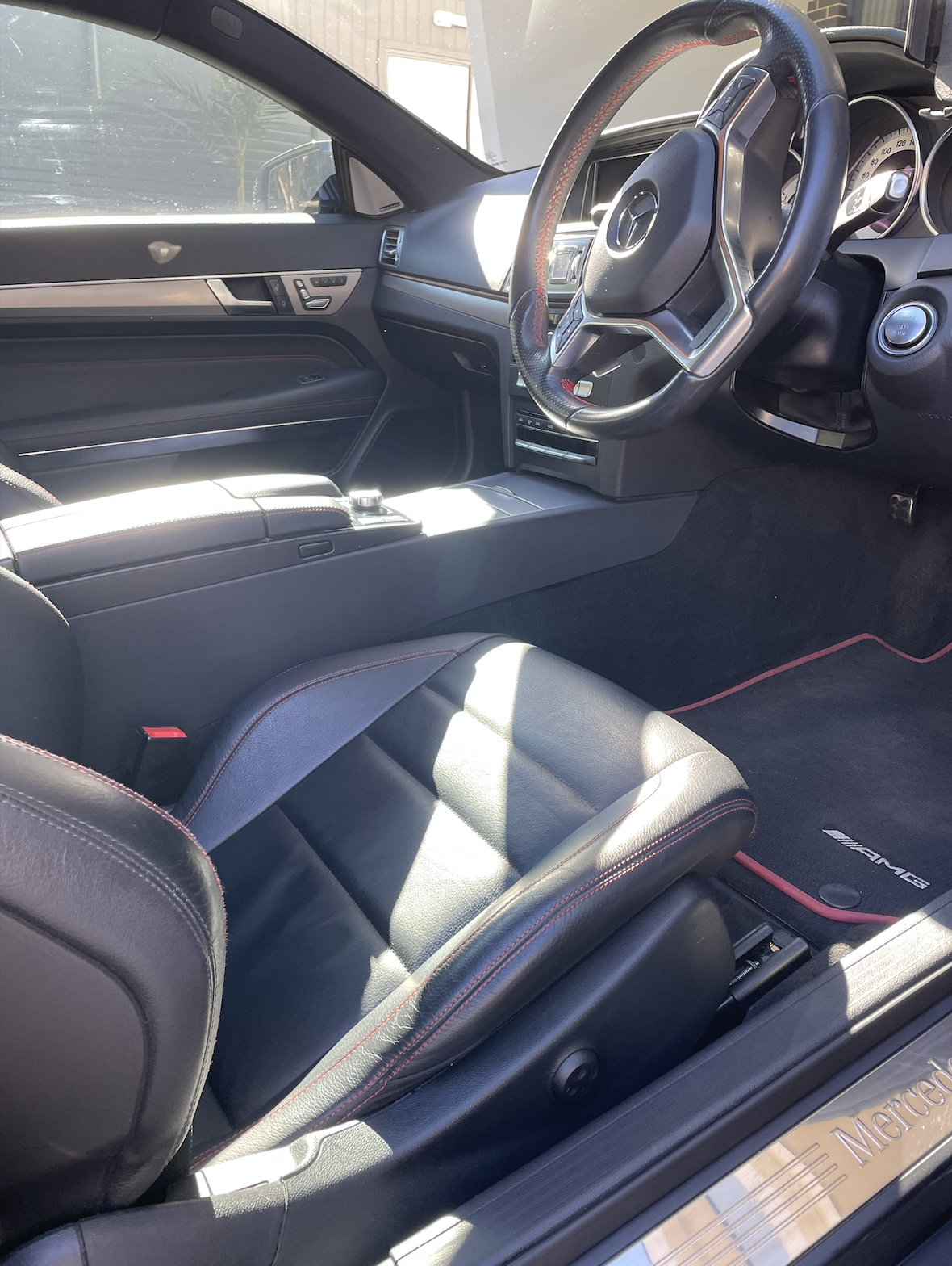 Interior of a Mercedes-Benz car showing the driver's seat, steering wheel, dashboard, and center console, with sunlight illuminating parts of the seat and interior.