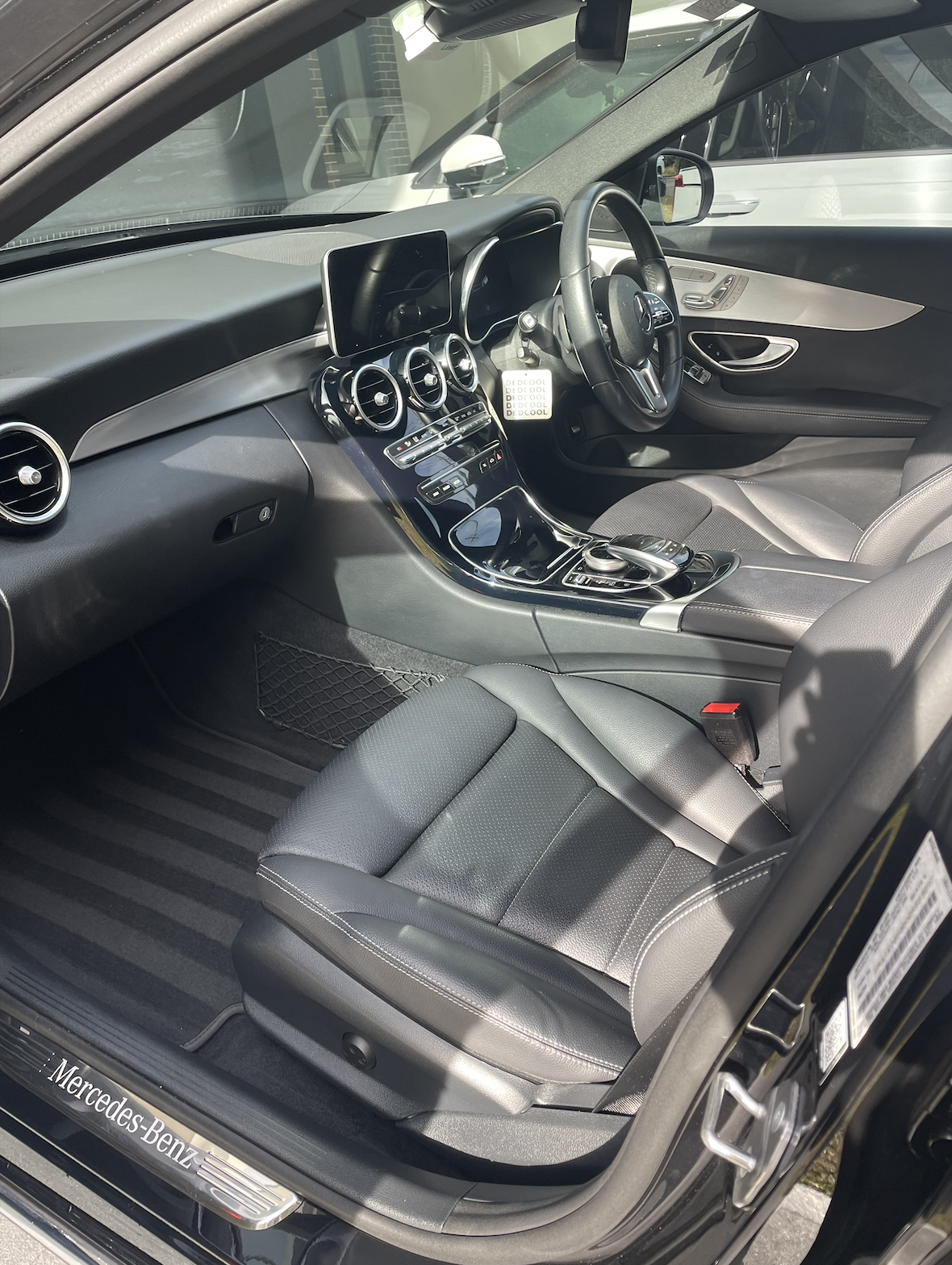 Interior of a black Mercedes-Benz car showing the dashboard, steering wheel, center console with control knob, and front seats.