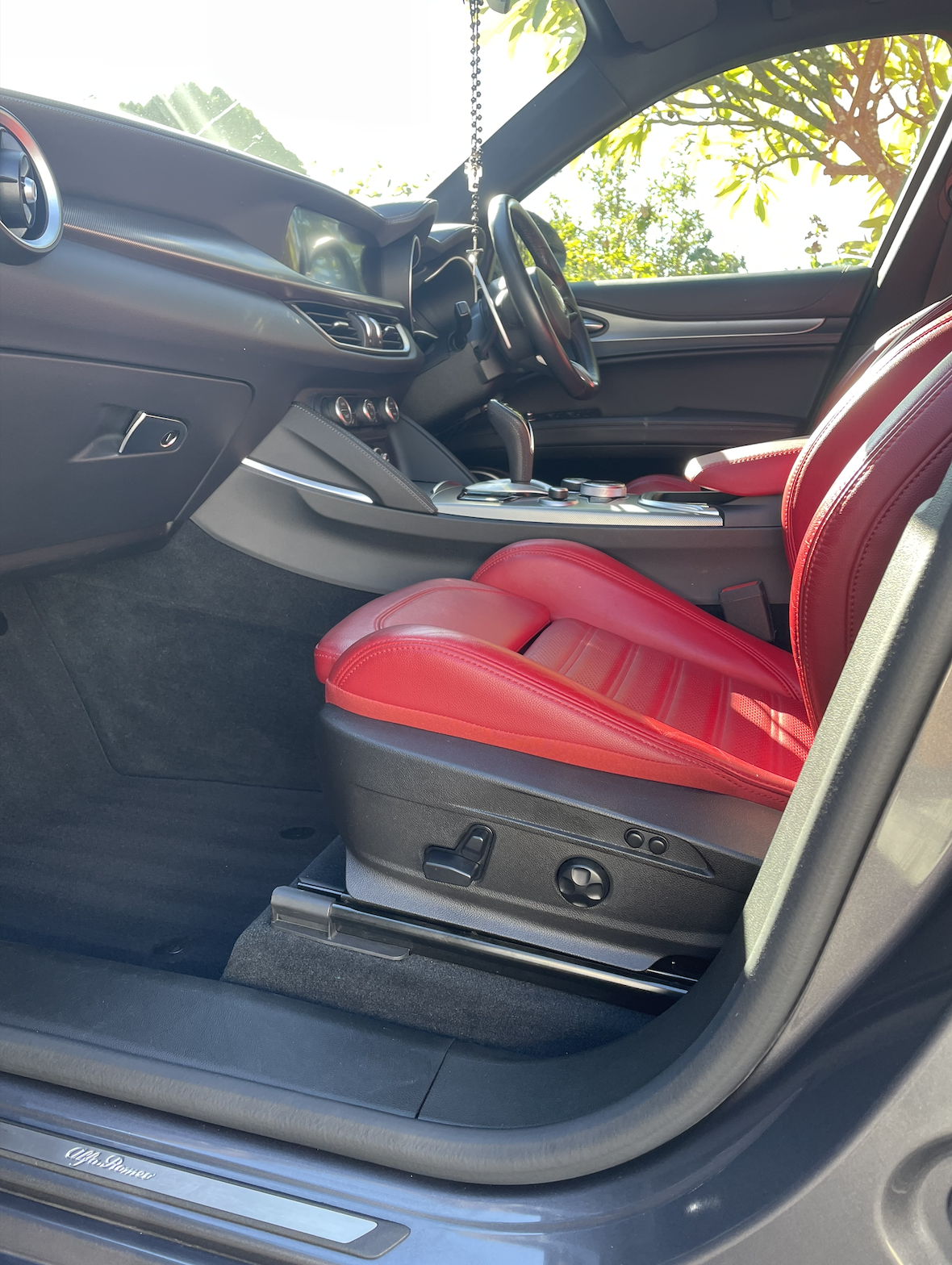 Interior of a car showcasing a red leather seat, steering wheel, dashboard, and center console with control buttons and gear shifter.
