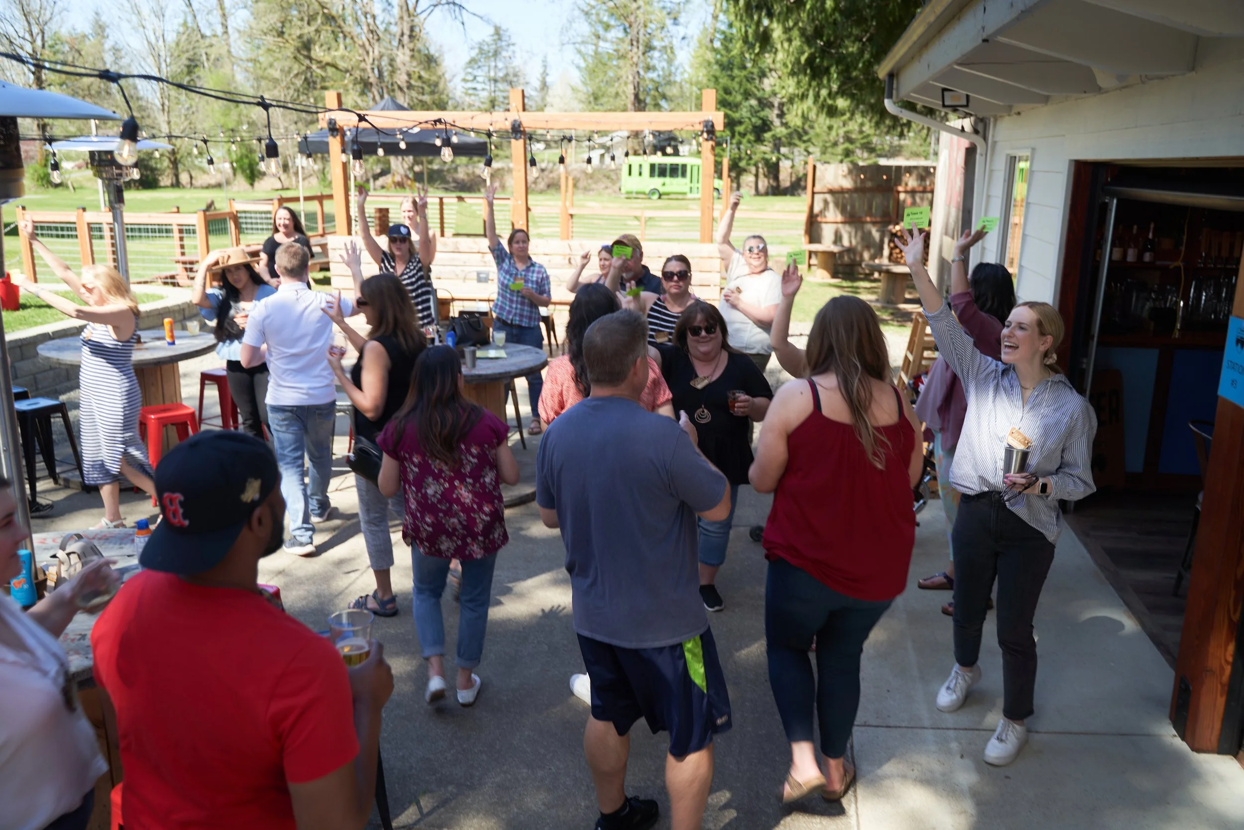 People dancing and socializing outside at a backyard party on a sunny day, with string lights hanging overhead.