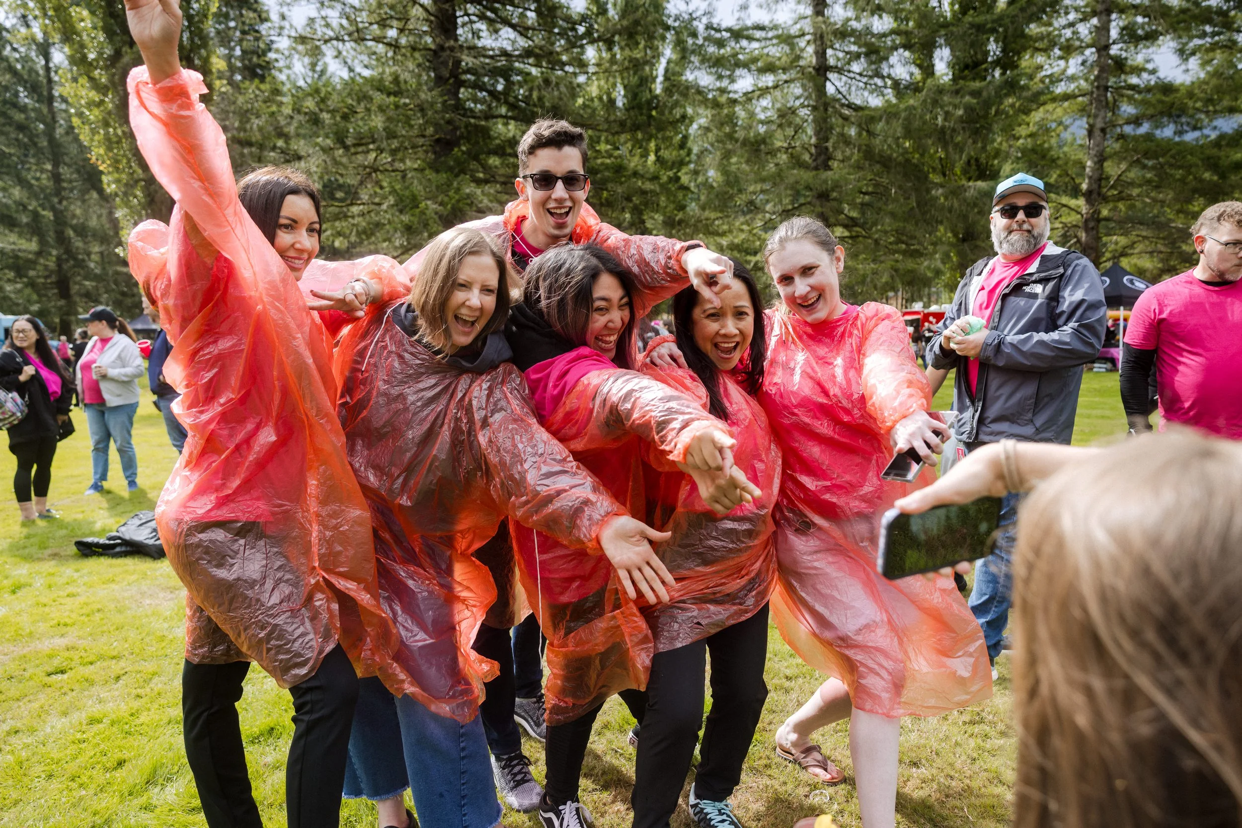 Group of people wearing colorful rain ponchos enjoying a playful outdoor gathering in a park.