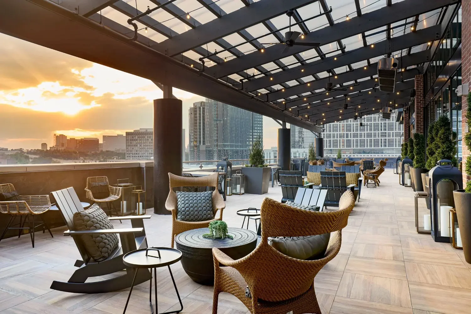 Rooftop lounge with modern outdoor furniture and city skyline at sunset.