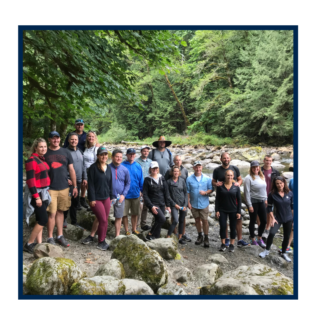 Group of people standing on rocks near a river in a forest after a team building hike.