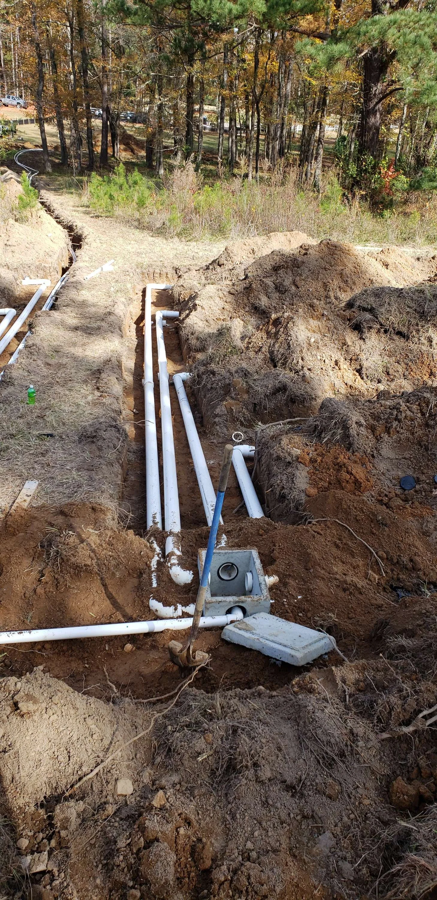 Underground piping installation in a dirt trench amidst a wooded area.