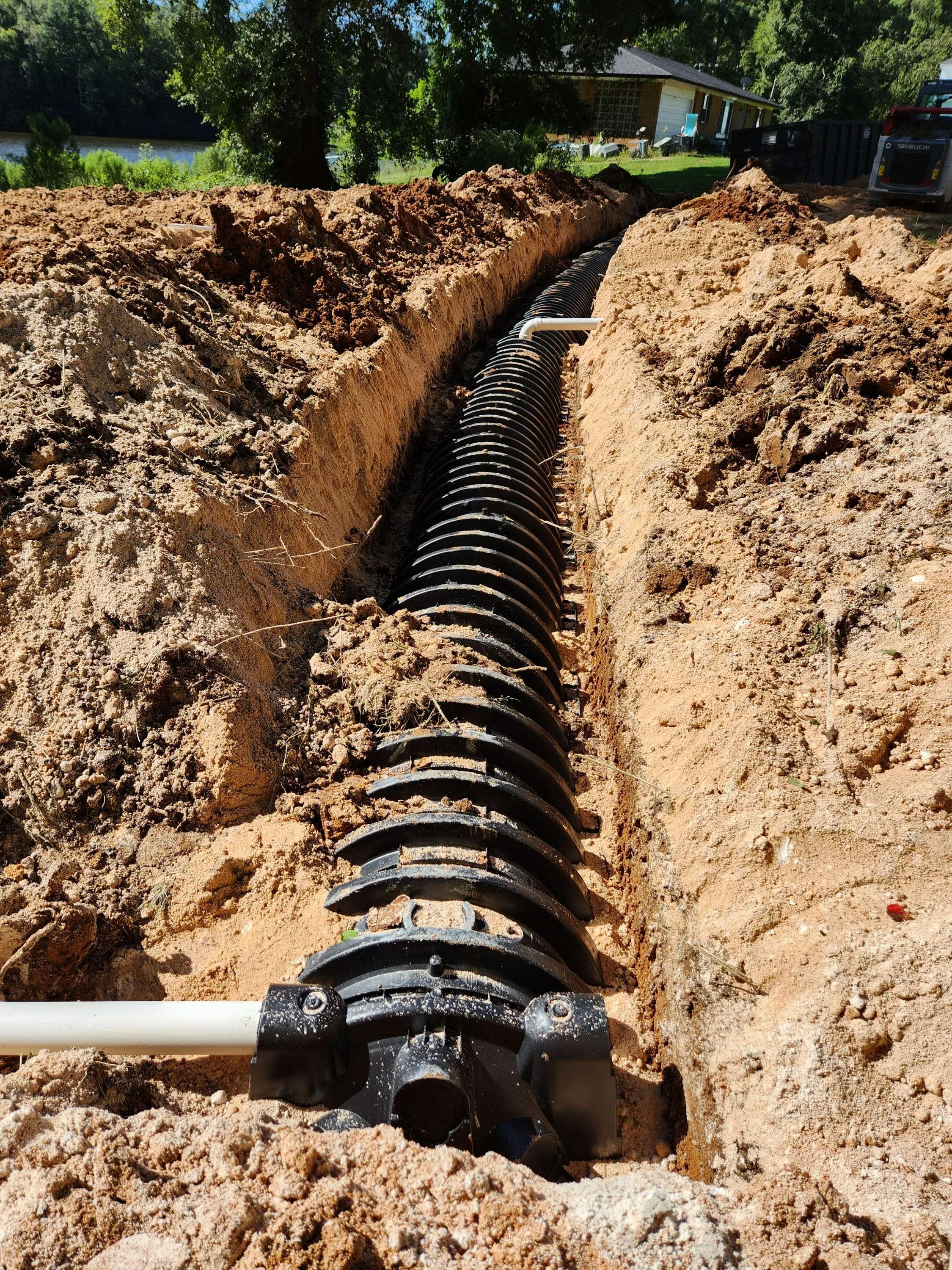 Installation of a black underground drainage pipe with a spiral structure in a trench during construction.