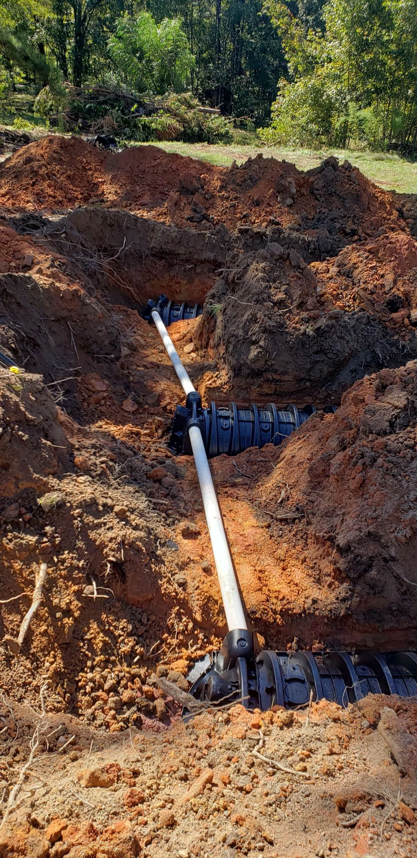 Underground pipe installation showing black flexible pipes, white PVC pipe, and orange dirt.